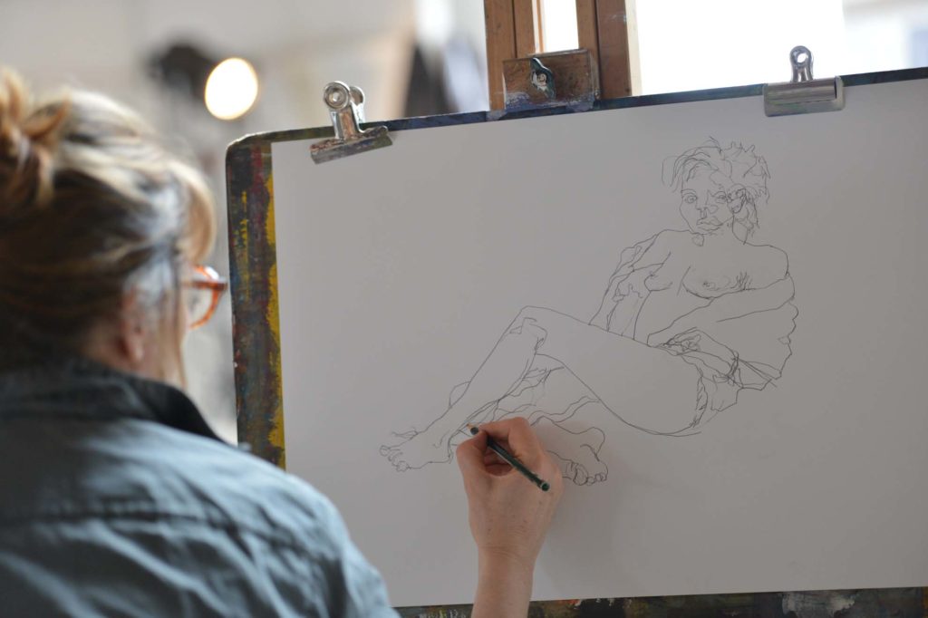 A lady drawing a figure seated at an an easel in Porthmeor Studios. St Ives. Life Drawing class.