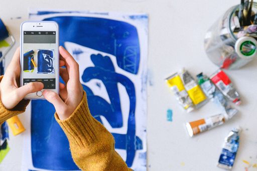 Someone using a smartphone to take a picture of a blue monoprint.